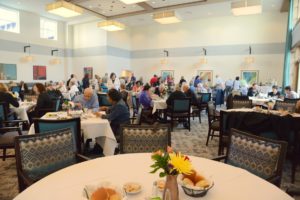 Wide view of a large community dining room filled with residents seated at tables.