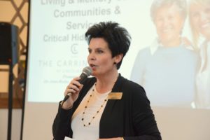 Woman speaking into a microphone during a presentation with residents seated nearby.