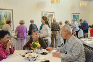 Residents seated at tables eating and talking during a communal meal.