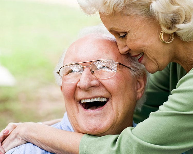 Older couple smiling and embracing outdoors, showing affection.