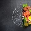 Healthy food packed with nutrition such as salmon, avocado, and nuts are stacked over the right side of a chalk drawing of a brain.