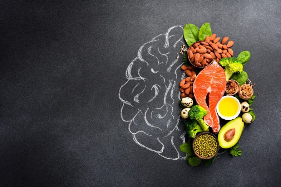 Healthy food packed with nutrition such as salmon, avocado, and nuts are stacked over the right side of a chalk drawing of a brain.