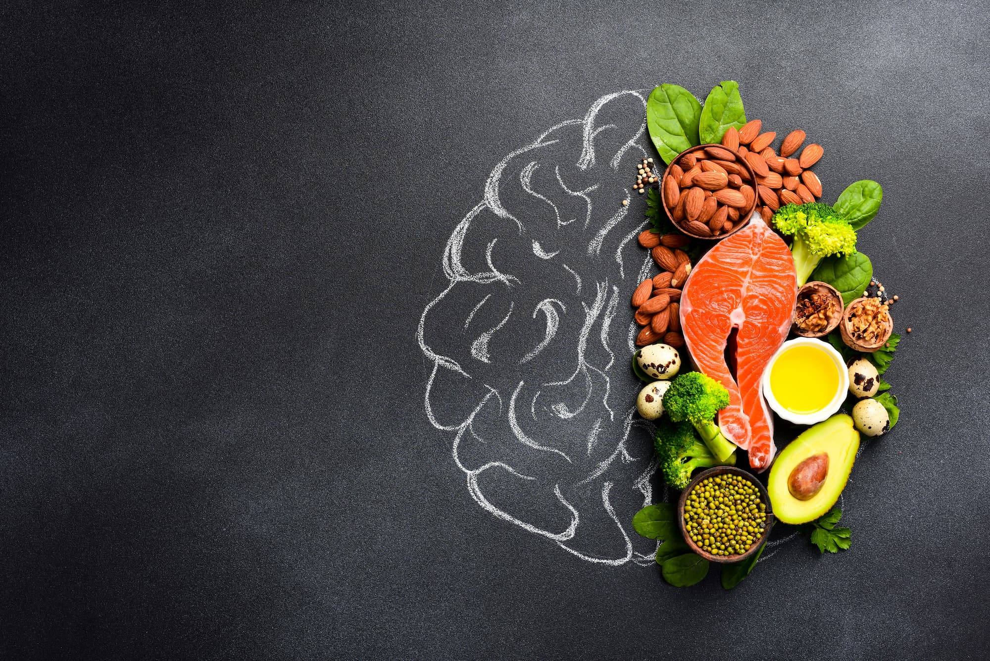 Healthy food packed with nutrition such as salmon, avocado, and nuts are stacked over the right side of a chalk drawing of a brain.