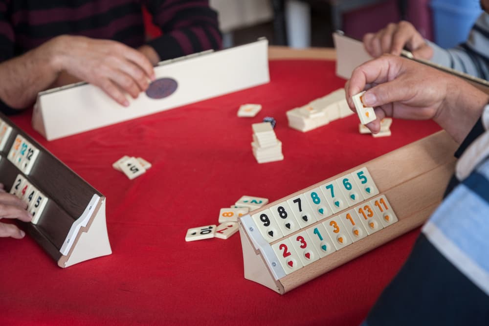 several seniors gather around a table playing a dominos game together.